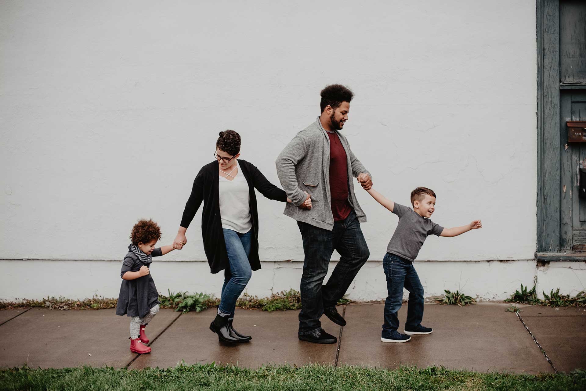 father mother and two children holding hands walking on a sidewalk