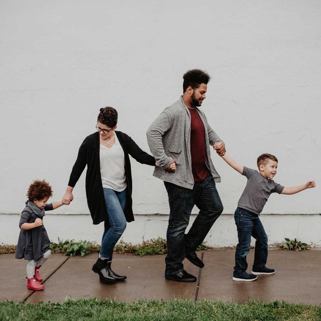 father mother and two children holding hands walking on a sidewalk